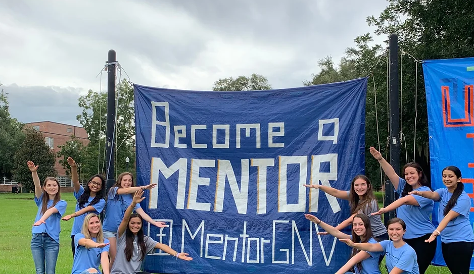 A group of MentorGNV members doing the gator chomp around a banner advertises MentorGNV.